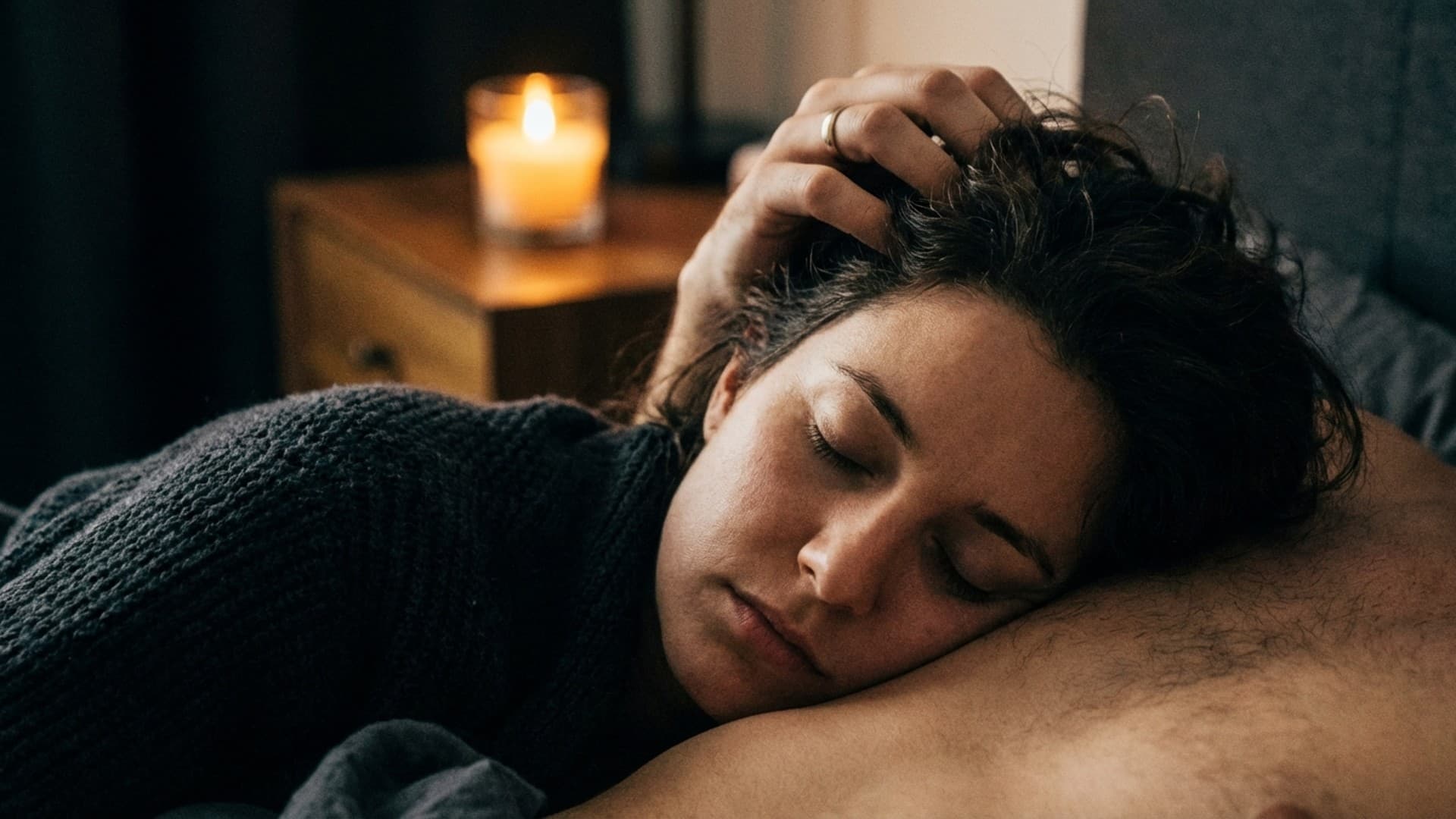 A close-up of someone resting peacefully against their partner's chest while their hair is gently stroked, in warm candlelight.