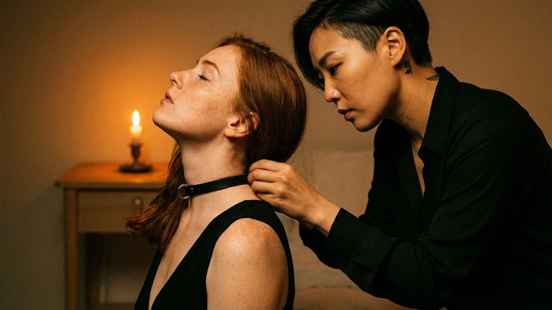 A woman fastens a leather collar on her partner, who tilts her head back with eyes closed, in warm candlelight.